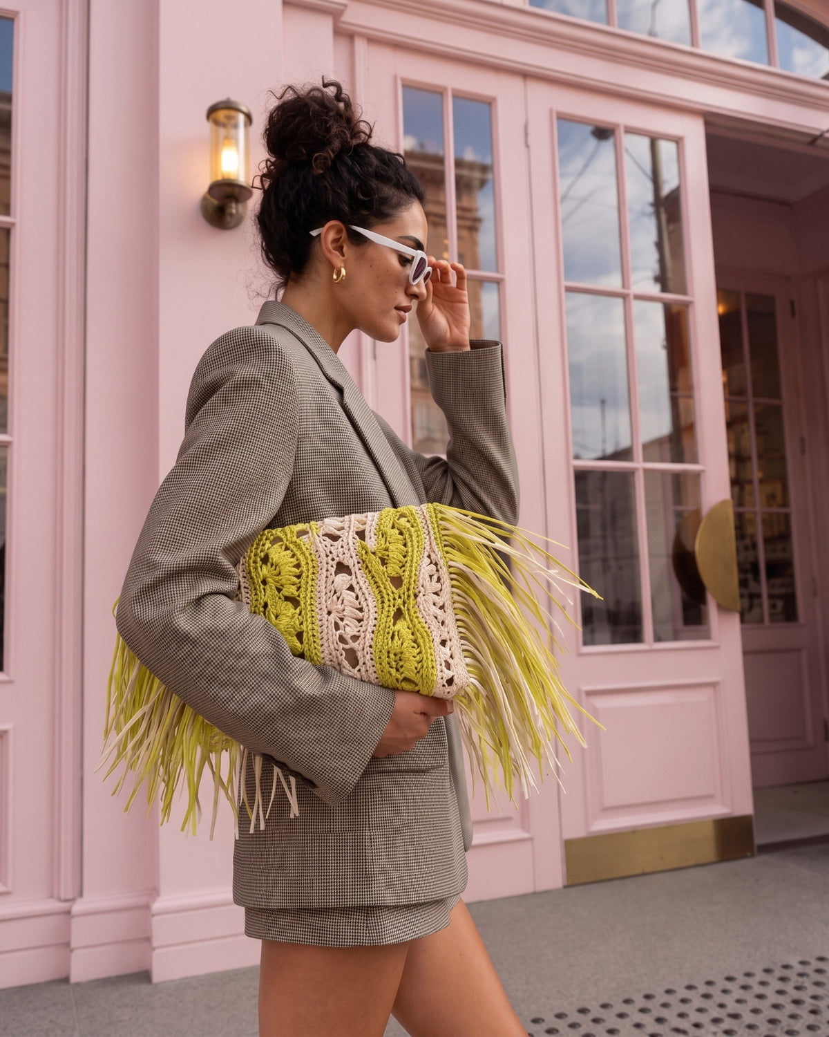 Woman carrying the Koukla SAGE handmade crochet clutch in chartreuse while walking past a pink building